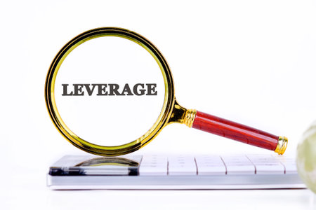 LEVERAGE text written through a magnifying glass, close-up on a calculator in front of a light backgroundの写真素材