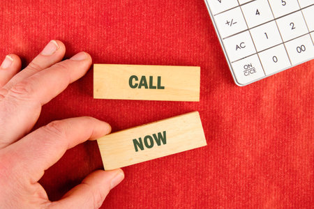 Conceptual call now symbol. Copy space. Call now message written made up of blocks with the help of a hand on a red backgroundの写真素材