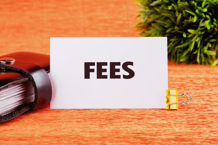 Business and finance concept. Costs, charges, commissions, penalties. Cost, fee and taxes. FEES on a white card on an orange background, close-up, front viewの写真素材
