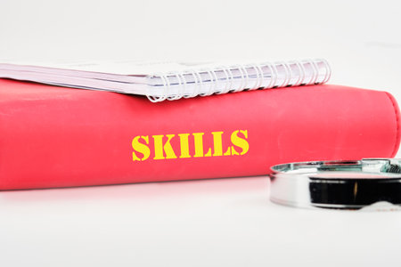 Upskilling and personal development concept. SKILLS words on the end of a business book, notebook on a white background.の写真素材