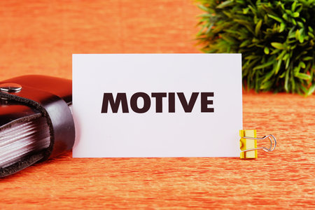 A card with the word motive prominently displayed sits beside a leather wallet and a small green plant on a bright wooden table.の写真素材