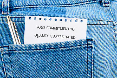 A folded note with a message of appreciation is tucked into the back pocket of a pair of denim jeans. A silver pen rests beside it, emphasizing the importance of quality.の写真素材