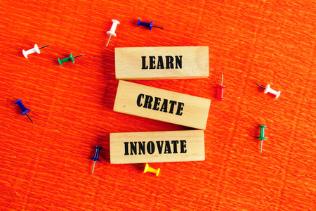 Three wooden blocks display the words learn, create, and innovate against an eye-catching orange background adorned with colorful push pins. This setup inspires creative thinking and growth.の写真素材