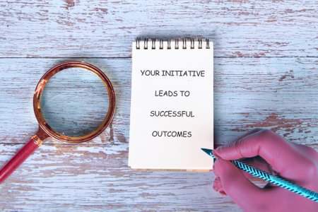 A hand writes on a notepad, emphasizing the message about successful outcomes stemming from initiative. A magnifying glass rests nearby, highlighting focus and clarity in work.の写真素材