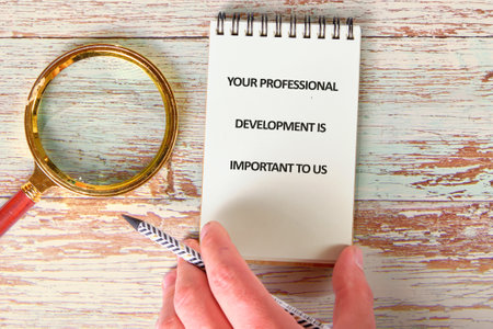 Notepad with a note highlighting the importance of professional development sits alongside a magnifying glass, illustrating focus on growth and learning.の写真素材