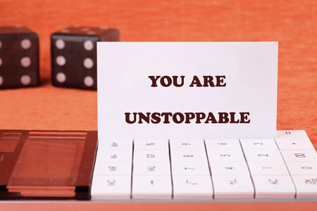 Concept text YOU ARE UNSTOPPABLE on a business card with game cubes in the background and a calculator in the foreground.の写真素材