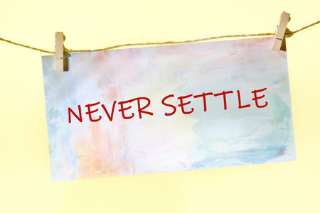 Concept words NEVER SETTLE written on a colorful sign on a rope with clothespins.の写真素材