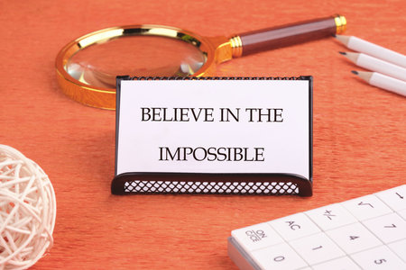 Motivational quote. BELIEVE IN THE IMPOSSIBLE text written on a business card on a black stand in front of an orange background.の写真素材