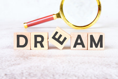 Dreams word written on wooden blocks placed next to a magnifying glass on a light textured background.の写真素材