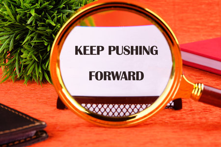 Concept text KEEP PUSHING FORWARD focuses through a magnifying glass on a business card on an orange background.の写真素材