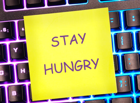 Concept Phase STAY HUNGRY written on a bright yellow sticker on a colorful keyboard.