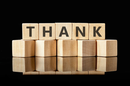 Appreciation concepts. Text THANK written on wooden cubes on a black reflective surface, emphasizes simplicity and elegance.の写真素材