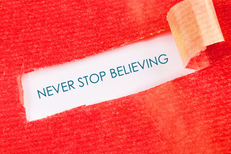 NEVER STOP BELIEVING motivational phrase under a piece of torn paper.の写真素材