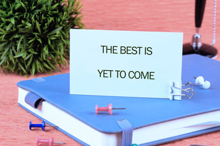 Motivational quotes THE BEST IS YET TO COME written on a card on a blue notebook next to colorful pins and an ornamental plant.の写真素材