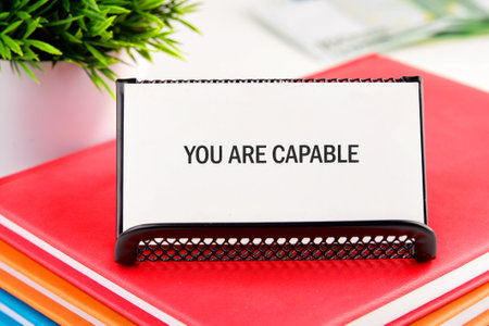 Business capable or incapable concept. Copy space. Motivational words YOU ARE CAPABLE on a white business card in a stand on a stack of notebooks.の写真素材