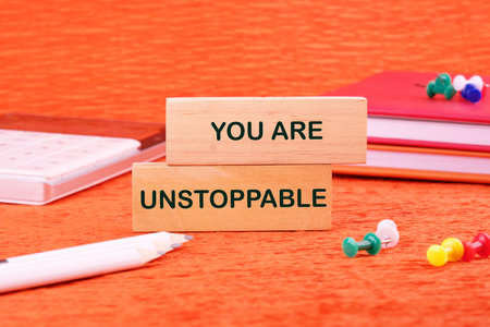 Concept text YOU ARE UNSTOPPABLE made of wooden blocks on an orange background with stationery lying next to it.の写真素材