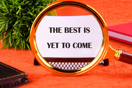 Motivational quotes THE BEST IS YET TO COME focuses through a magnifying glass on a business card on an orange background.の写真素材