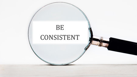 Business concept text BE CONSISTENT focused through a magnifying glass.の写真素材