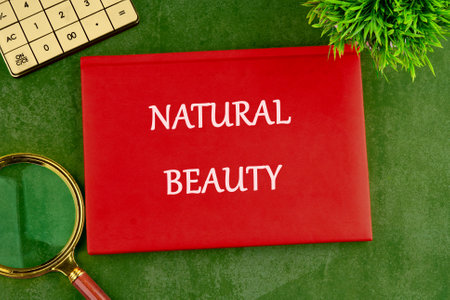 A striking display featuring the words natural beauty on a vivid red background. Surrounded by a magnifying glass and green foliage, the setting inspires reflection and appreciation for nature.の写真素材