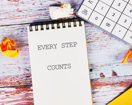 Concept text EVERY STEP COUNTS written on a blank notebook that lies on a wooden surface next to a...