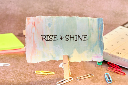 Growth Success Achievement Progress Concept. Words RISE AND SHINE written on paper, fixed in a clothespin