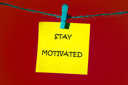 Support, motivation, psychological concept. STAY MOTIVATED written on a bright yellow note, which is attached to the shoelace with a blue clothespin on a bright red background.の写真素材