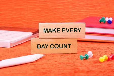 Concept words MAKE EVERY DAY COUNT made of wooden blocks on an orange background with stationery lying next to it.の写真素材