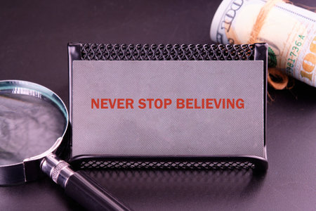 NEVER STOP BELIEVING motivational phrase close-up on a gray business card.
