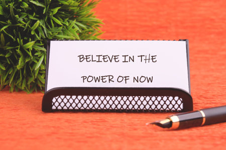 Finance and business concept. Text BELIEVE IN THE POWER OF NOW written on the business card holder....