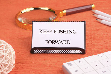 Concept text KEEP PUSHING FORWARD written on a business card on a black stand in front of an orange background.の写真素材