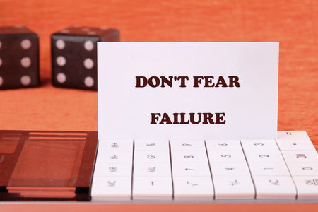 Concept text DO NOT FEAR FAILURE on a business card with game cubes in the background and a calculator in the foreground.の写真素材