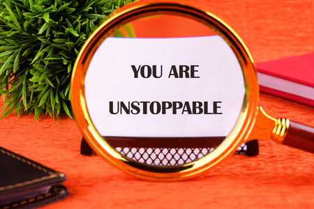 Concept text YOU ARE UNSTOPPABLE focuses through a magnifying glass on a business card on an orange background.の写真素材