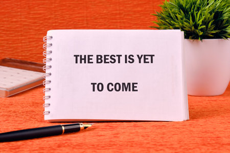Motivational quotes THE BEST IS YET TO COME on a spiral notebook on an orange background.