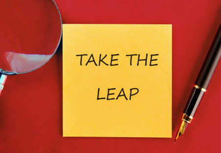TAKE THE LEAP WORDS WRITTEN on a yellow sticker on a red background, top view.