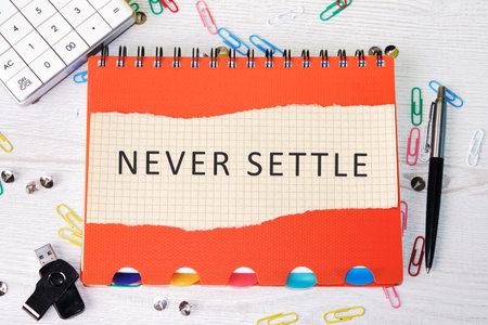 Concept words NEVER SETTLE written on paper on a colorful notebook.