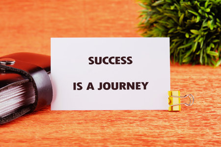 Concept text SUCCESS IS A JOURNEY written on a card on a bright orange table next to a black...