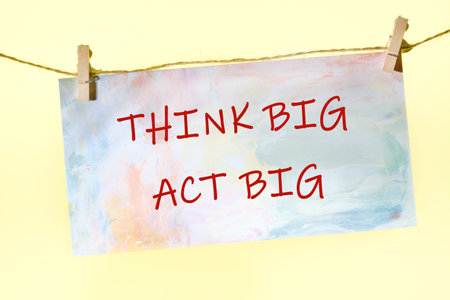 THINK BIG ACT BIG concept words written on a colorful sign on a rope with clothespins.