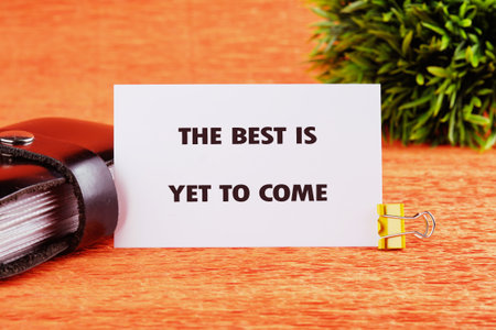 Motivational quotes THE BEST IS YET TO COME written on a card on a bright orange table next to a...