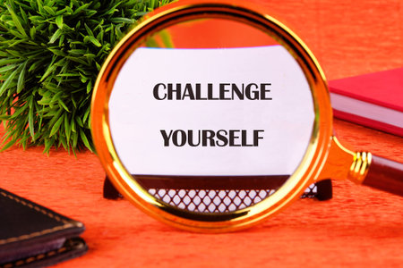 Believe in yourself, overcoming challenges concept. CHALLENGE YOURSELF text focuses through a magnifying glass on a business card on an orange background.の写真素材
