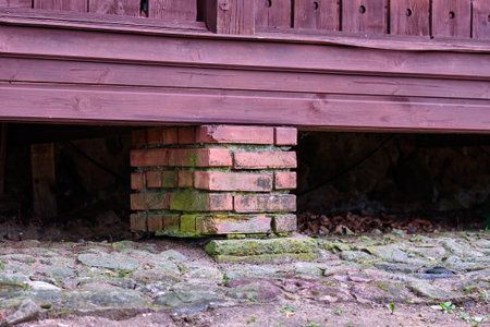 Close-up view of a brick support under a wooden building, showcasing moss-covered bricks and natural elements in a rustic environment.の写真素材