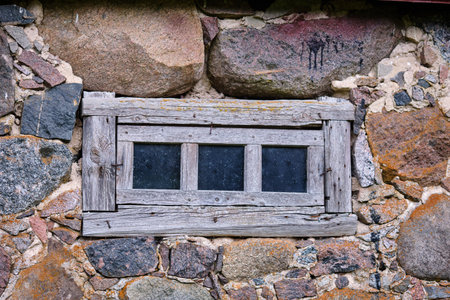 A weathered wooden window is set within a rugged stone wall, showcasing the craftsmanship and...