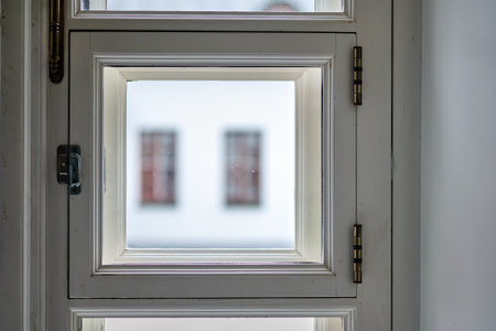 Wooden window frame displays a soft focus of a building facade, reflecting natural light, creating a...