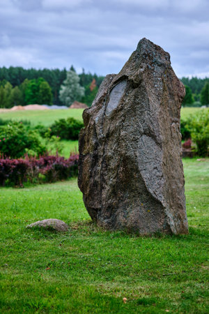 Large stone standing alone in a green field during an overcast day near lush trees and bushesの写真素材