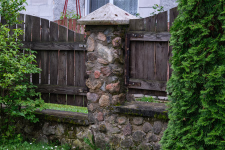 A rustic stone wall supports a wooden gate in a peaceful garden with greenery surrounding the...