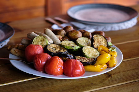 Delicious grilled vegetables like zucchini, eggplant, and peppers are served alongside sausages,...