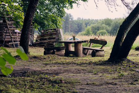 A wooden table and benches sit under trees, creating a peaceful gathering spot in a serene forest...