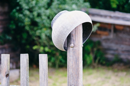 A weathered metal cooking pot is overturned on a wooden fence post. The setting shows a rural or agricultural atmosphere during the daytime.の写真素材