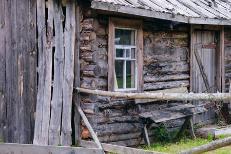 An old log cabin shows a weathered exterior with a window, door, and makeshift table. A rough wood...