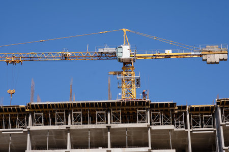 A building under construction has a large crane above it. A construction worker stands on the top...