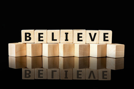 The concept word BELIEVE has been collected of wooden cubes on a glossy black background. Business believe concept. Copy spaceの写真素材